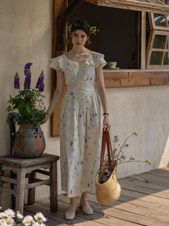 Woman standing by a rustic window, wearing a cottagecore floral dress with flutter sleeves, holding a woven basket filled with wildflowers next to a vintage vase of lupines.