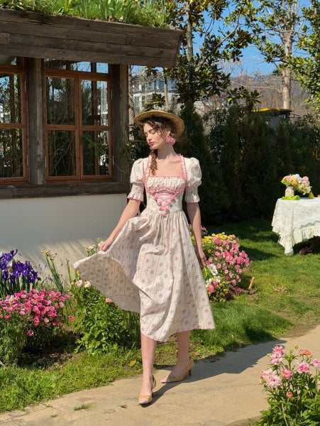 A romantic outdoor scene with a woman twirling in a cottagecore floral dress with puffed sleeves and pink ribbon accents, surrounded by blooming flowers and a rustic house in the background.