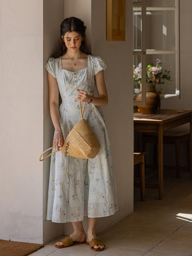 Delicate floral dress with button-down front and vintage-style cap sleeves, styled in a rustic dining scene, capturing a relaxed, fairytale-inspired afternoon with grapes and a glass of sparkling drink.