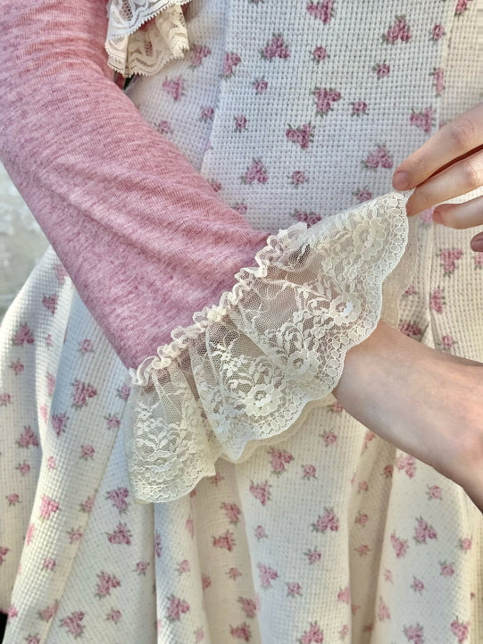 Close-up of the lace-trimmed sleeve on a pink cardigan, showcasing intricate floral lace details and soft, feminine textures over a vintage-inspired floral dress with a waffle knit texture.