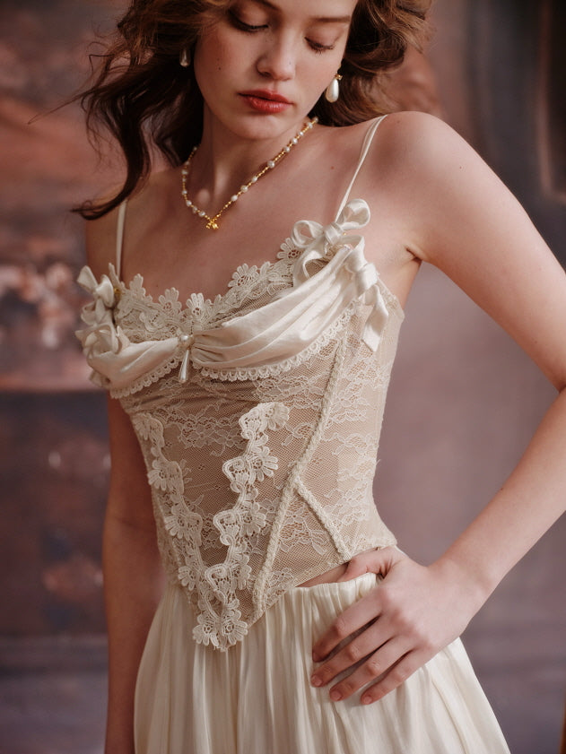 A close-up of an ivory lace corset with satin ribbon bows and floral embroidery, styled in a romantic fairytale look with pearl accessories and softly curled hair.