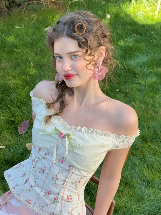 Close-up of floral embroidered off-shoulder corset top with lace trim and green ribbon detail, styled with pink satin skirt in a romantic spring garden – fairytale cottagecore fashion