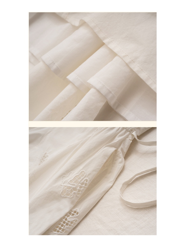 A close-up of the tiered hem of a white embroidered dress, showing the intricate lace patterns and flowing silhouette.