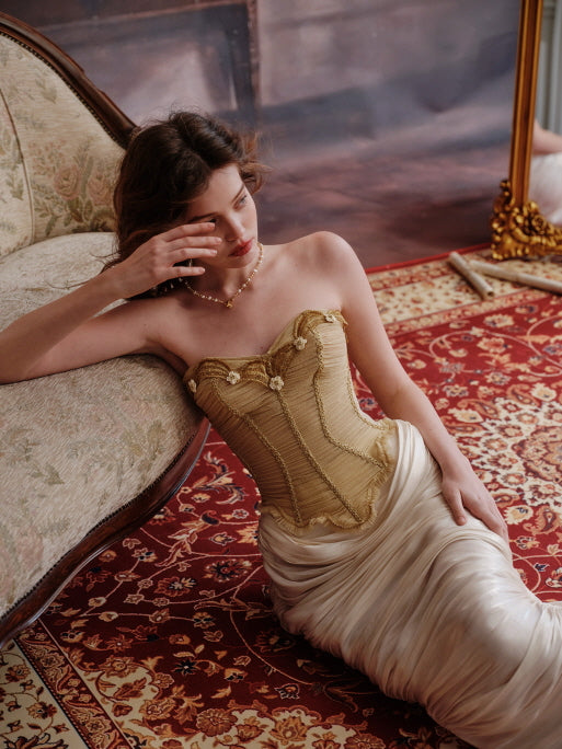 A dreamy romantic outfit with a gold structured corset and ivory ruched skirt, styled in a luxurious vintage setting with red floral carpet and antique furniture, evoking soft fairytale elegance.