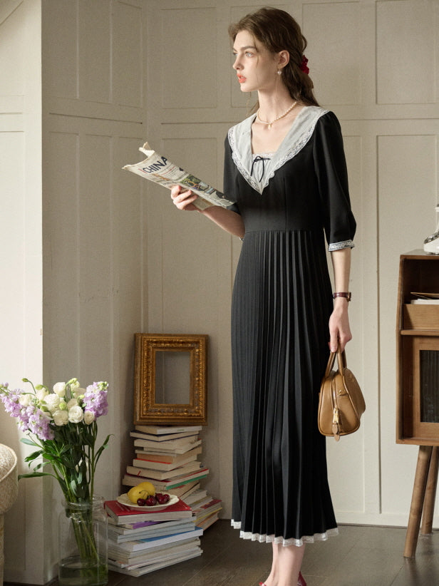A woman in a retro black dress with a lace-trimmed collar and pleated skirt, styled for an elegant and casual outfit with fairytale charm in a cozy reading nook.