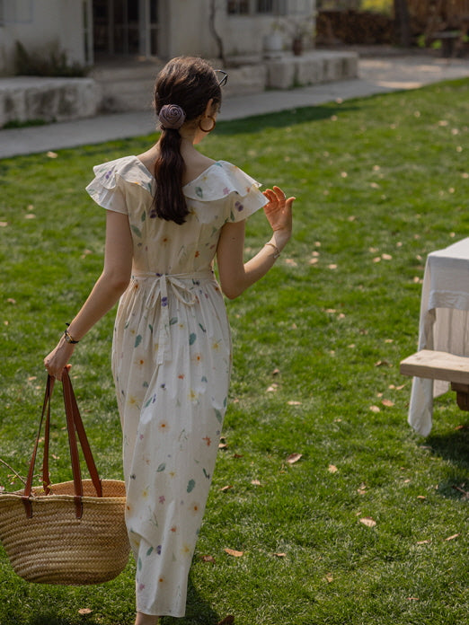 Rear view of a woman in a cottagecore floral dress with ruffled sleeves, carrying a straw basket and strolling through a garden, exuding a relaxed, vintage-inspired atmosphere.