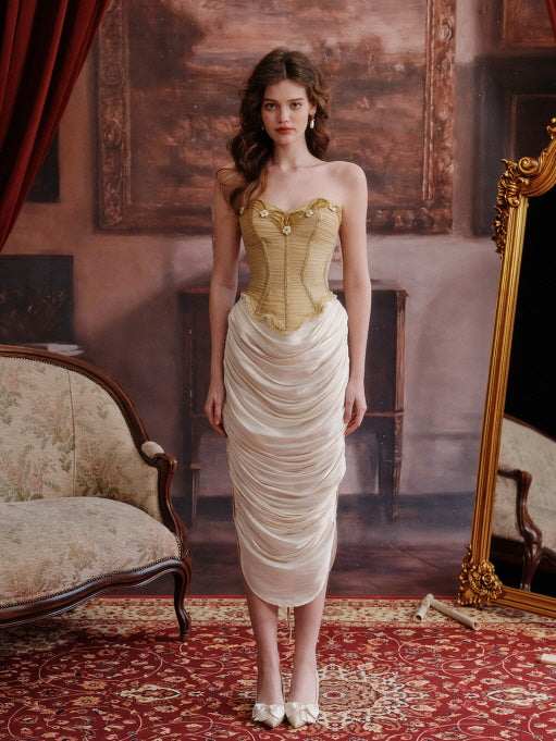 Cream ruched satin midi skirt styled with a structured golden corset top and bow heels, photographed in an antique room – romantic vintage-inspired women’s fashion