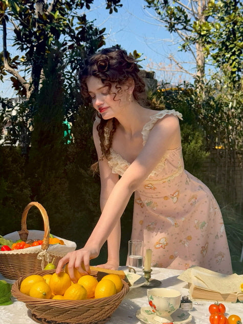 Romantic cottagecore dress adorned with floral lace and delicate ruffle straps, as a young woman arranges a basket of lemons in a dreamy picnic scene.
