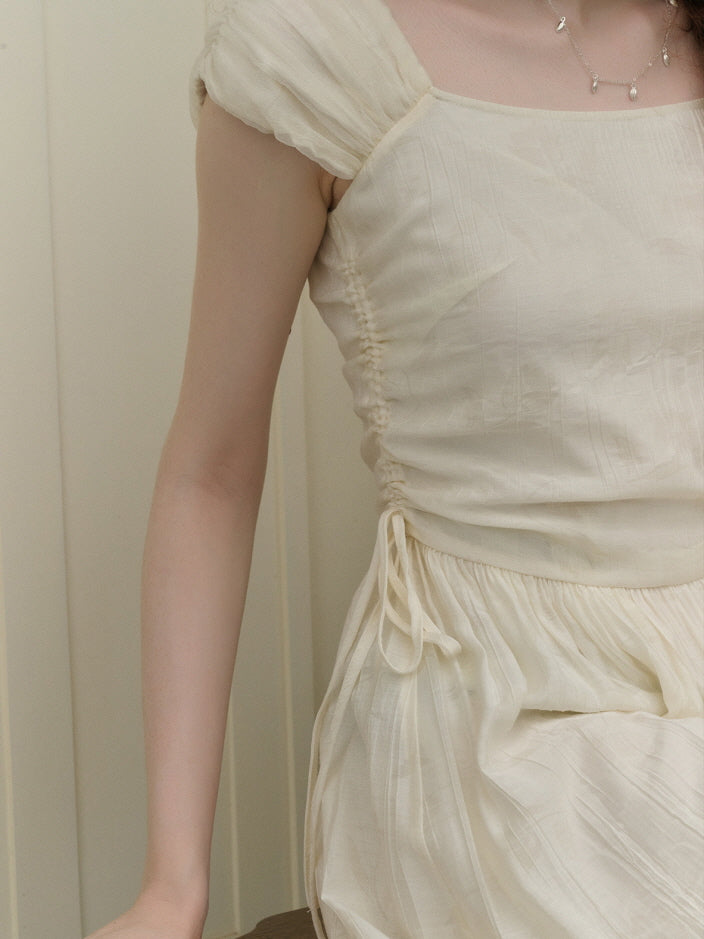 Close-up of the side ruching and delicate sleeve detail of an ivory textured dress, highlighting the gathered waist and soft, lightweight fabric.