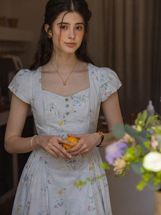 Romantic floral dress with cap sleeves and buttoned bodice, styled in a soft, vintage-inspired kitchen setting, capturing a gentle, fairytale ambiance with delicate flower patterns.