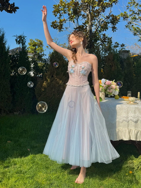 Woman in a pastel blue tulle corset dress with floral embroidery, playing with soap bubbles in a garden – dreamy fairytale fashion for spring or summer