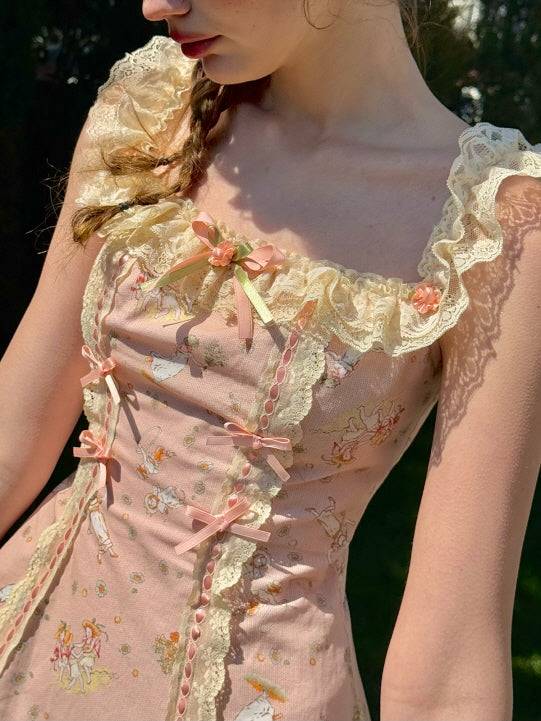 Close-up of a pink vintage-style dress with lace trim and pastel bows, adorned with whimsical fairytale illustrations, creating a delicate, cottagecore aesthetic.