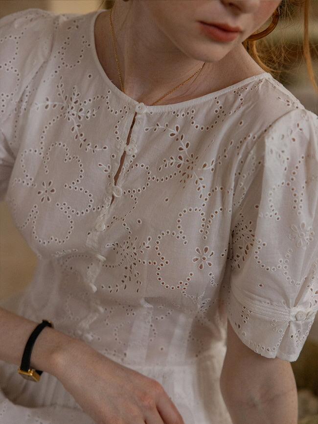 Close-up of a woman wearing a white eyelet lace dress with floral embroidery and puff sleeves, exuding vintage cottagecore charm.