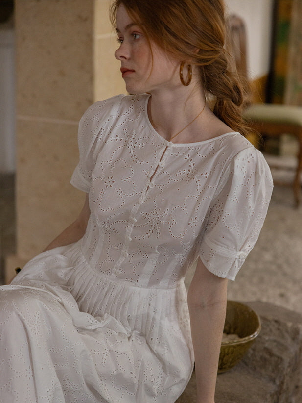 Side view of a woman sitting gracefully in a white eyelet lace dress with puff sleeves and floral embroidery. Vintage-inspired, romantic look.