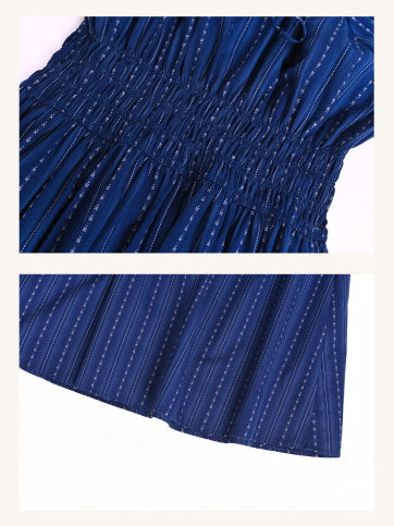 Close-up of the smocked waist and hemline of a navy blue dress with delicate vertical stripe patterns. Highlights the gathered texture and soft, flowy fabric detail.