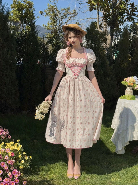 A young woman in a puff-sleeved vintage floral dress with ribbon details stands gracefully in a flower-filled yard, holding a small bouquet, embodying the soft and feminine charm of Romantic Fairytale style.