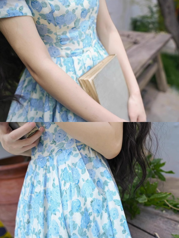 Close-up of a blue floral dress with a fitted waist and delicate floral print, styled with a vintage book and evoking a charming cottagecore aesthetic.