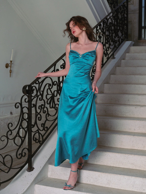A woman poses on a grand staircase in a flowing turquoise satin dress, her hand gently holding the hem — ethereal evening look, vintage princess style, dreamy fairytale aesthetic.