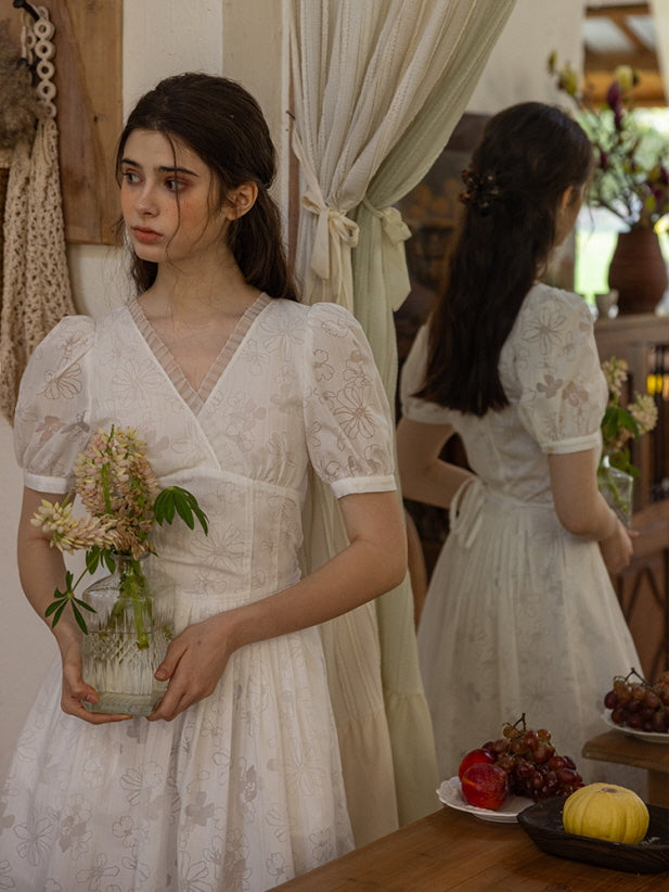 Rustic wooden cabinet with a vintage-inspired white floral mini dress featuring delicate puff sleeves and a pleated skirt, creating a romantic cottagecore aesthetic.