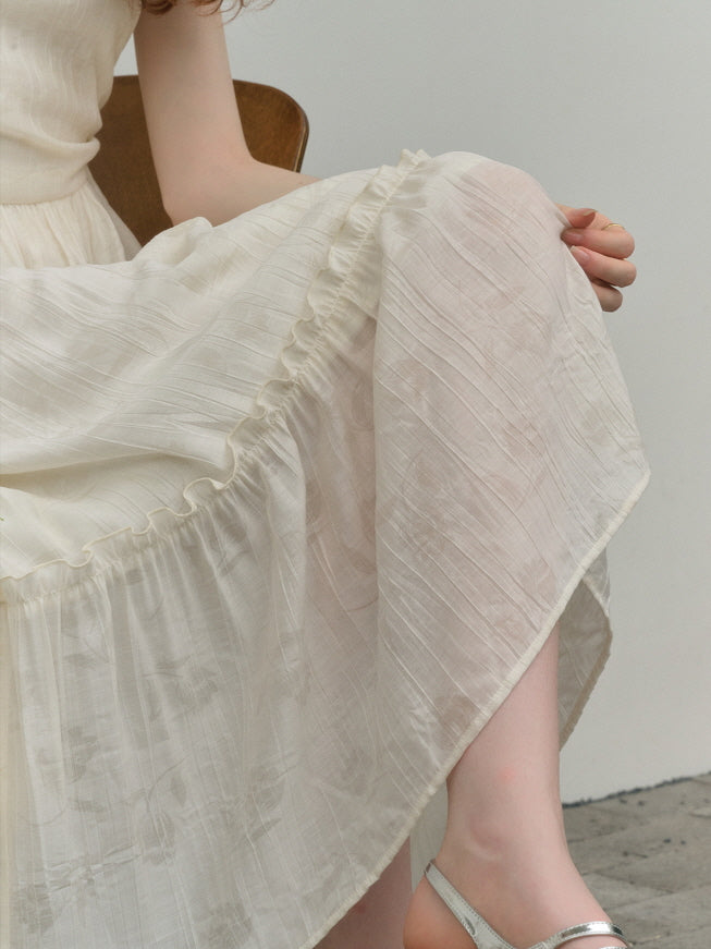 Close-up of an ivory dress showcasing delicate textured fabric and soft gathered ruffles along the skirt hem, highlighting the lightweight and airy material with a subtle floral pattern.
