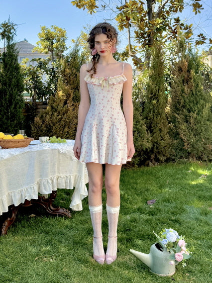 Full-length view of a pink floral dress with lace accents, styled with knee-high lace socks and soft pink heels in a garden setting.