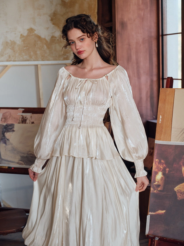 Romantic vintage-style satin blouse with puff sleeves and ruched waist, styled with a flowing cream skirt in an elegant art studio setting.