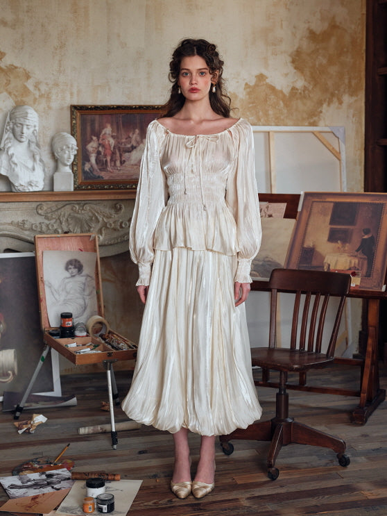 Close-up of an elegant ivory satin blouse with long puff sleeves and gathered waist, styled with a cream balloon hem skirt, set in a vintage artist's atelier.