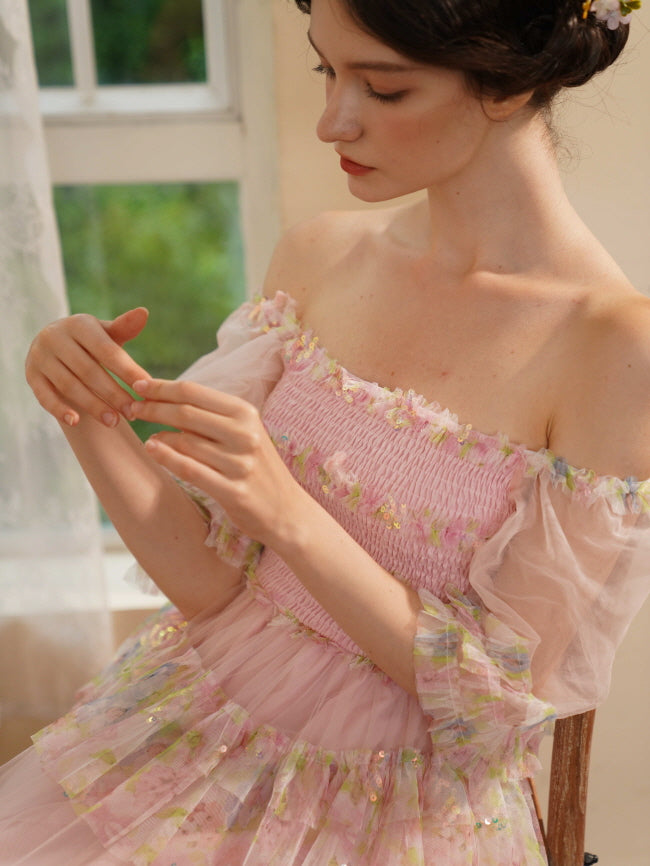 A woman in a pink off-shoulder tulle dress with floral details gently touches her fingers, evoking a soft fairycore and romantic aesthetic.