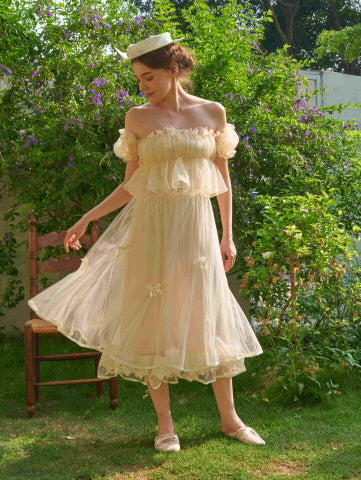 A model twirls in a flowy ivory skirt adorned with satin bows and lace hem, styled with a fairycore sheer top in a dreamy garden setting.