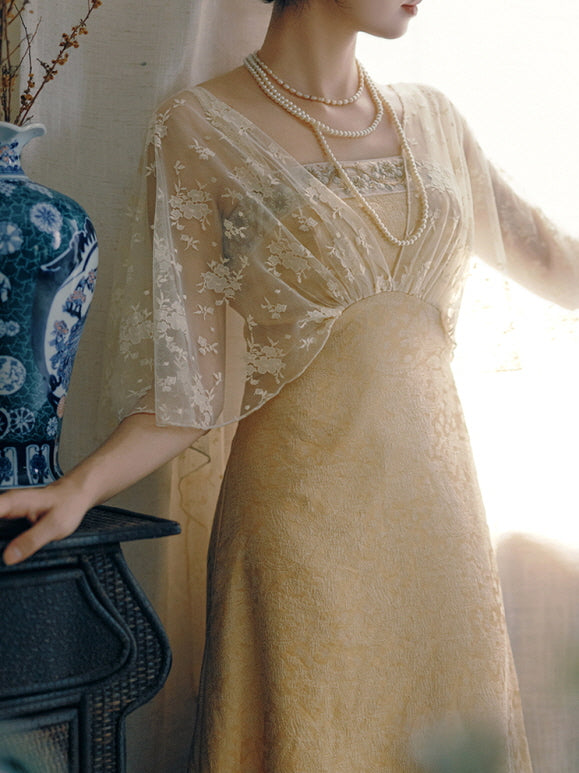 A woman in a vintage-inspired gold jacquard dress with sheer floral cape stands by the window, radiating timeless fairycore elegance.