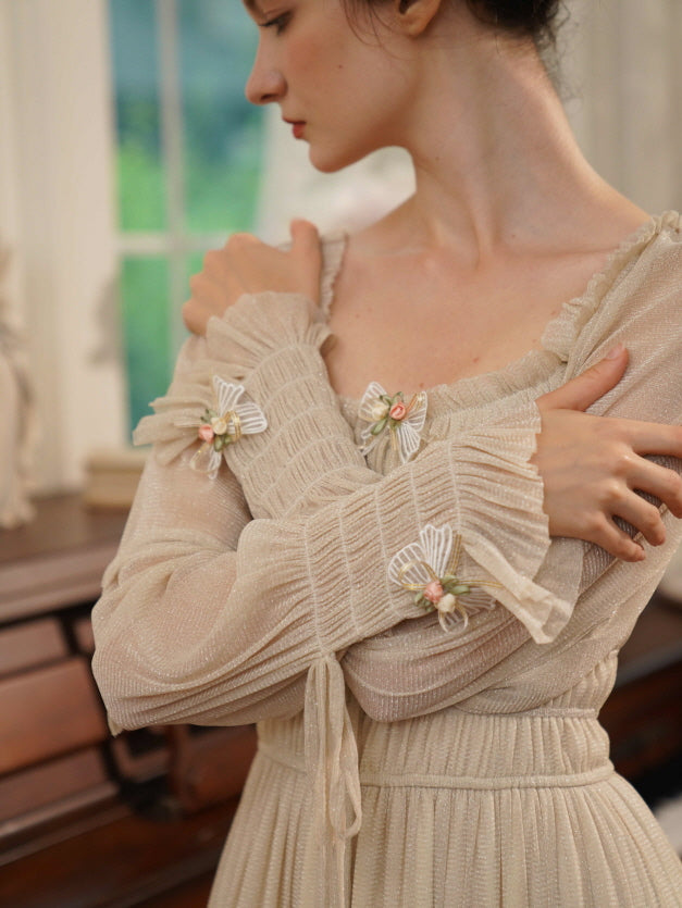 A woman in a cream vintage-style dress with floral ribbon accents crosses her arms softly, capturing a romantic and nostalgic mood.