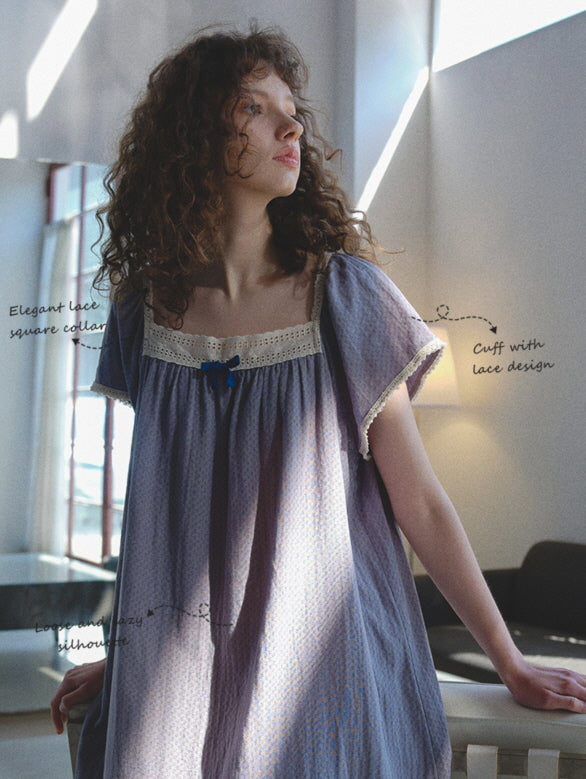 A young woman stands in soft sunlight wearing a lavender nightgown with a lace square collar and ribbon detail, evoking a dreamy cottagecore mood.