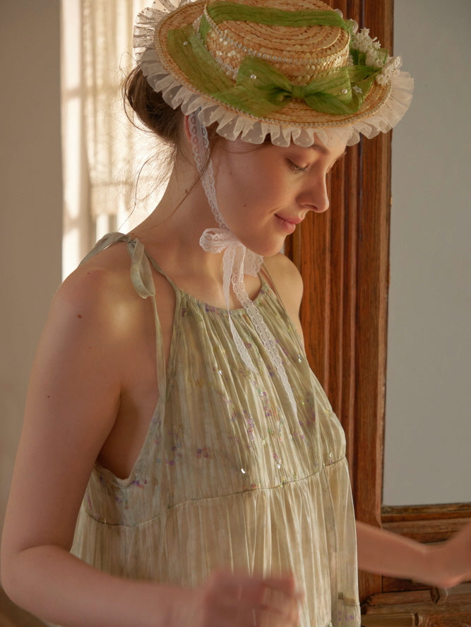 A woman in a pastel green halter dress smiles softly in vintage lighting, wearing a lace-trimmed straw bonnet for a fairycore cottage look.