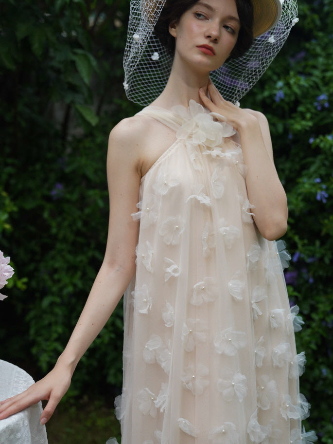 Close-up of a model wearing a beige halter dress with 3D flower embellishments, exuding soft fairycore elegance in a lush garden.