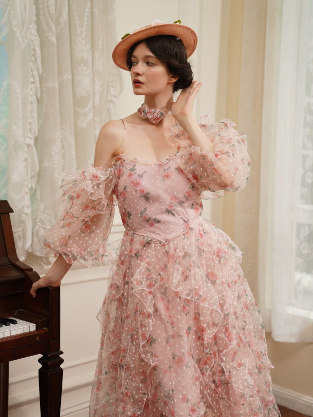 A woman in a ruffled pink floral mesh dress stands beside a piano, styled with a vintage hat and rose choker for a dreamy fairytale look.