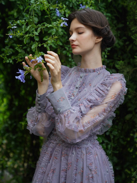 In a sheer lavender floral dress, the model gazes at soft blue blooms, capturing a serene and ethereal fairycore moment in the garden.