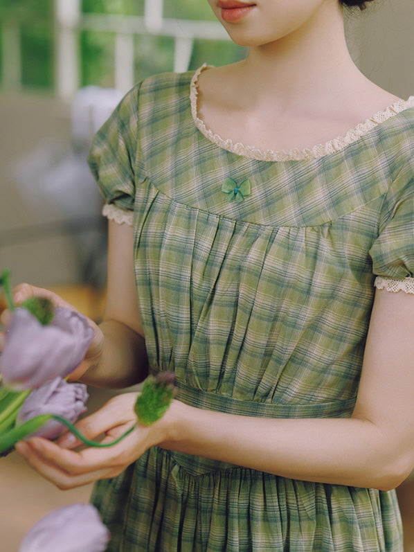 A close-up of a green plaid dress adorned with lace trim and a small embroidered bow at the neckline. The airy, princesscore style evokes a romantic, timeless feel, perfect for a fairytale-inspired aesthetic.
