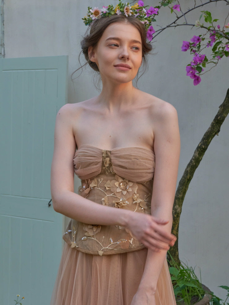 Model wears a romantic embroidered corset dress with floral crown, capturing soft princesscore vibes in a serene cottage garden setting.