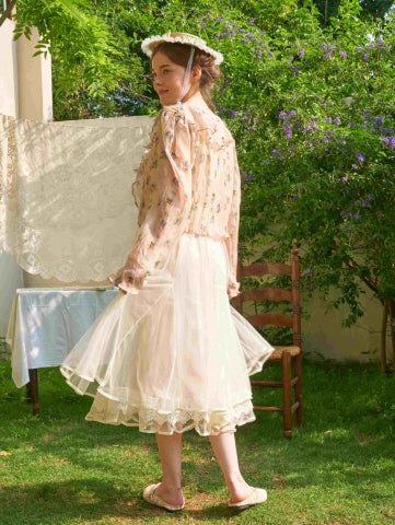 Seen from behind, the model pairs a sheer embroidered blouse with a layered ivory skirt, creating a whimsical and romantic princesscore outfit.