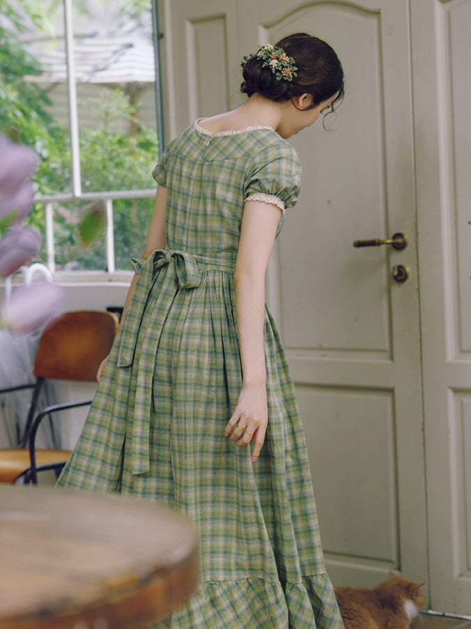 The model gracefully walks away, revealing the charming back bow and flowing tiered hem of the green plaid dress, exuding a fairytale-like, princesscore vibe.