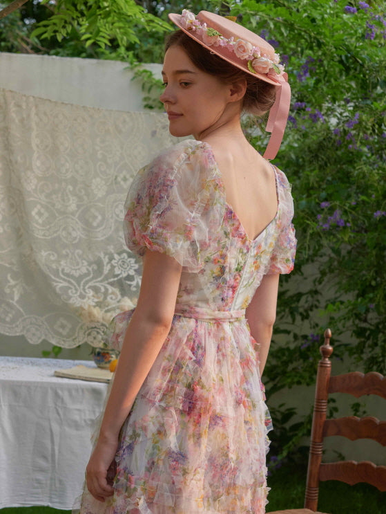 The woman stands in a garden wearing a V-back floral puff-sleeve dress, her pink bonnet adorned with flowers for a romantic vintage touch.