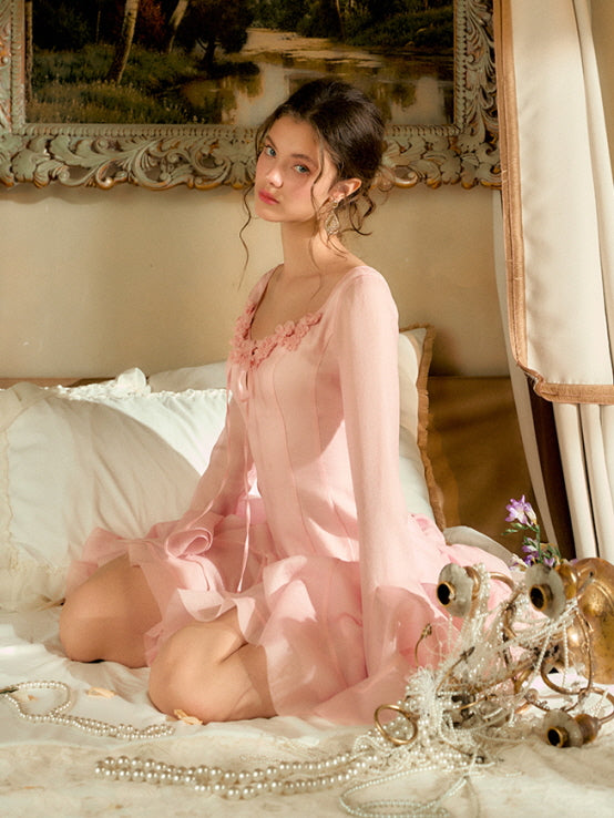 A model in a soft pink coquette princesscore dress sits gracefully on the bed, surrounded by pearls and flowers in a dreamy, vintage room.