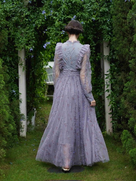 The model walks through a floral archway in a flowing lavender dress, capturing a wistful fairytale mood from behind in a cottage garden.