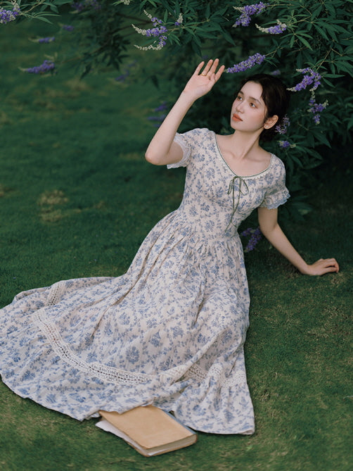 The model reclines on the grass, basking in the sunlight while wearing a flowy, vintage-style floral dress with lace accents, evoking a dreamy, nostalgic vibe.