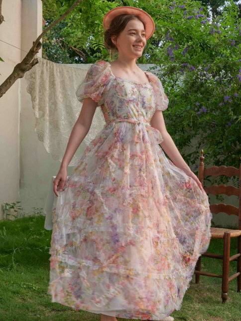 Smiling in a layered floral dress with ribbon waist and soft puff sleeves, the woman lifts the hem gently, glowing with fairycore elegance.