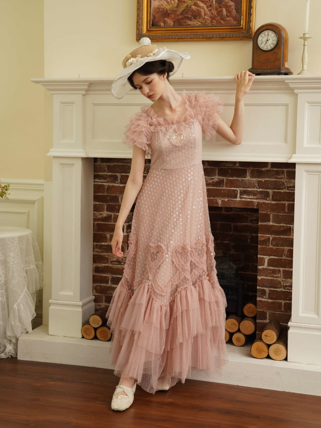 Model posing gracefully in a pink ruffle mesh dress with heart details, styled in a vintage room. A romantic princesscore aesthetic.