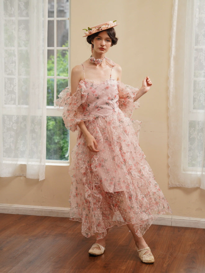 A woman in a romantic pink floral ruffle dress poses gracefully by a sunlit window, exuding soft elegance and vintage charm.