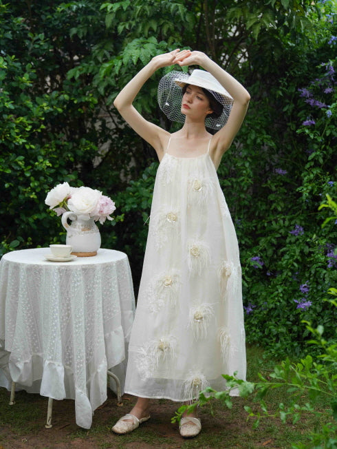 Model stretches gracefully in a flowy cream dress with floral feather appliqués, capturing a soft and dreamy fairycore garden moment.