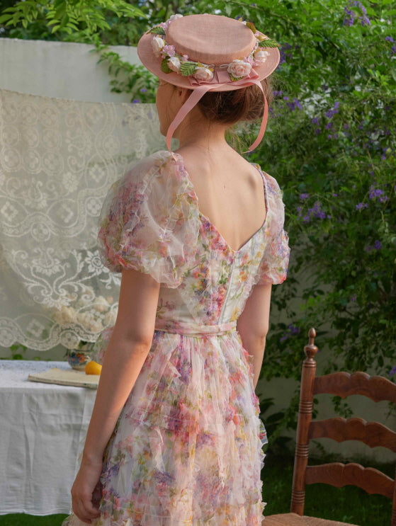 Back view of a woman in a pastel floral dress with puff sleeves and layered tulle, her bonnet adorned with pink roses for a cottagecore touch.