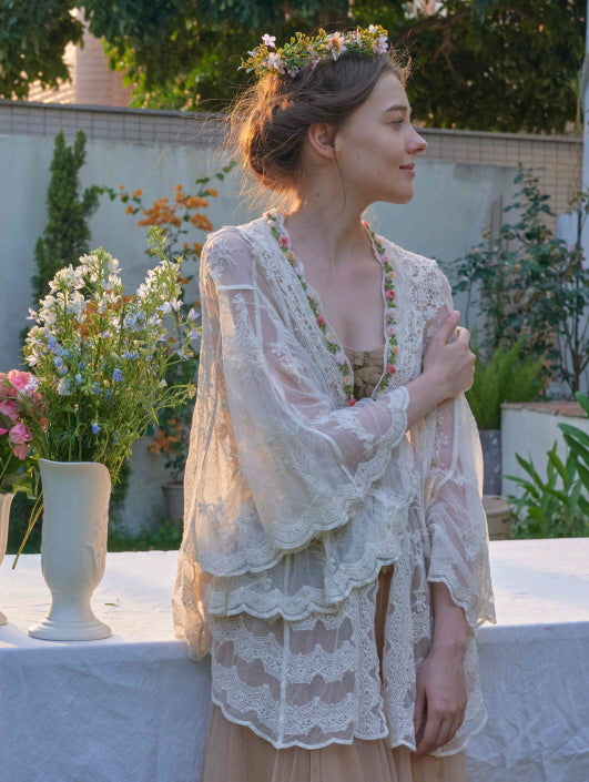 Close-up of a romantic lace cape with floral embroidery, worn over a corset dress, captured in golden hour light with fairycore styling.